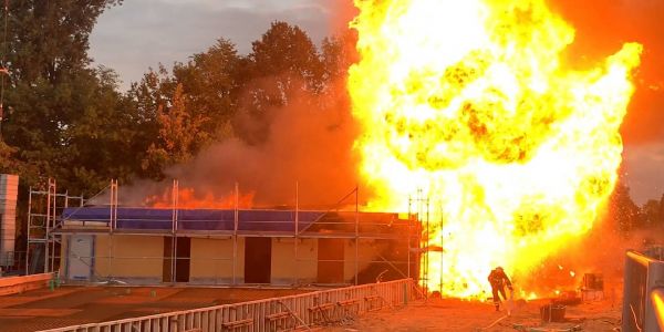 Eine der Gasflaschen explodiert. Ein Feuerwehrmann geht in Deckung. Foto: Mücahid Güler Feuer in Rohbau beim SV Wilhelmsburg: Es sollte das Vereinsheim werden