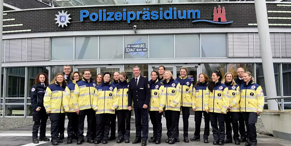 Polizeivizepräsident Mirko Streiber (Mitte) mit den neuen Mitgliedern und Ausbildern des Hamburger DRK-Kriseninterventionsteams auf den Treppen des Polizeipräsidiums.  © DRK Hamburg-Harburg 2025