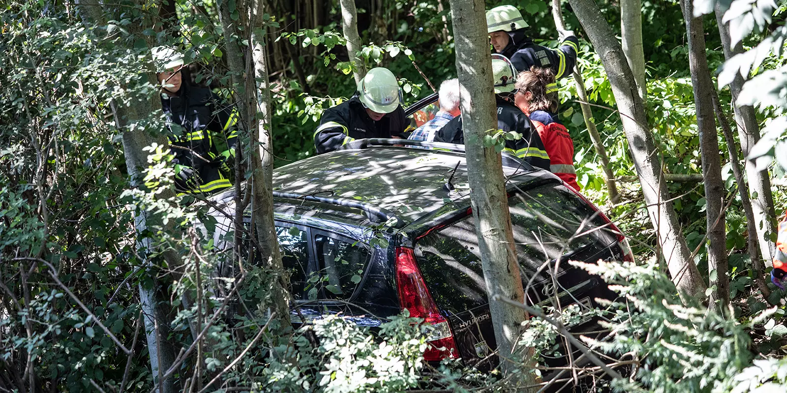 Feuerwehrleute holen den Fahrer aus dem zwischen Bäumen stehenden Auto. Foto: zv
