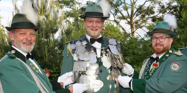 Die Adjus Holger Schlüter (links) und Stefan Schubert hängen König Sebastian Schröder die Königskette an. Foto: Christian Bittcher