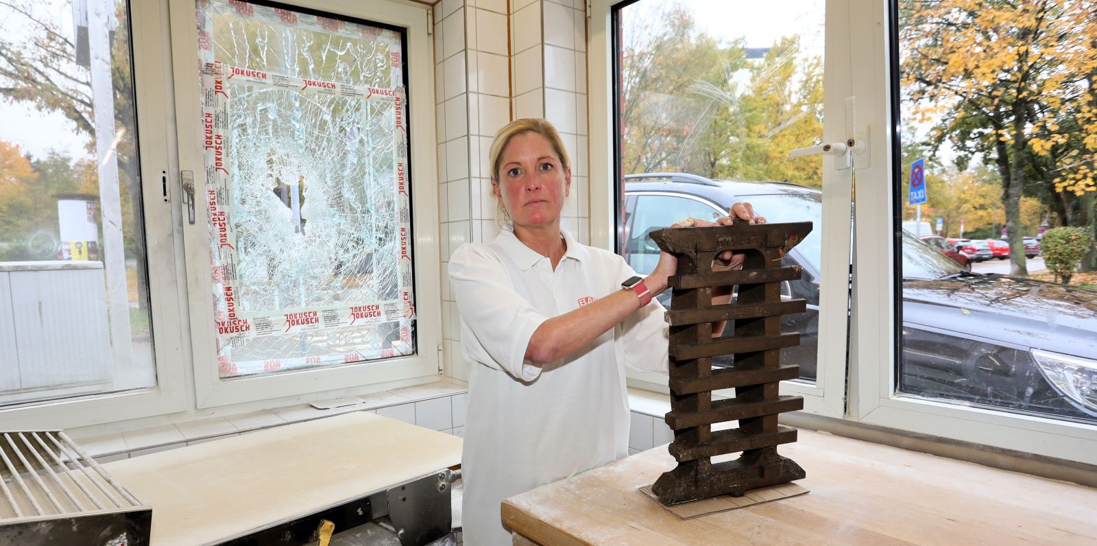 Wiebke Krüger mit dem Gullydeckel an der zerstörten Scheibe der Backstube. Foto: Christian Bittcher